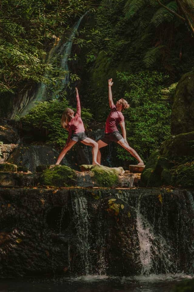 Couple Practicing Yoga By Tropical Waterfall