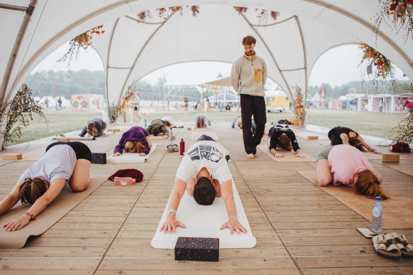 Group yoga class in child's pose under a festival tent