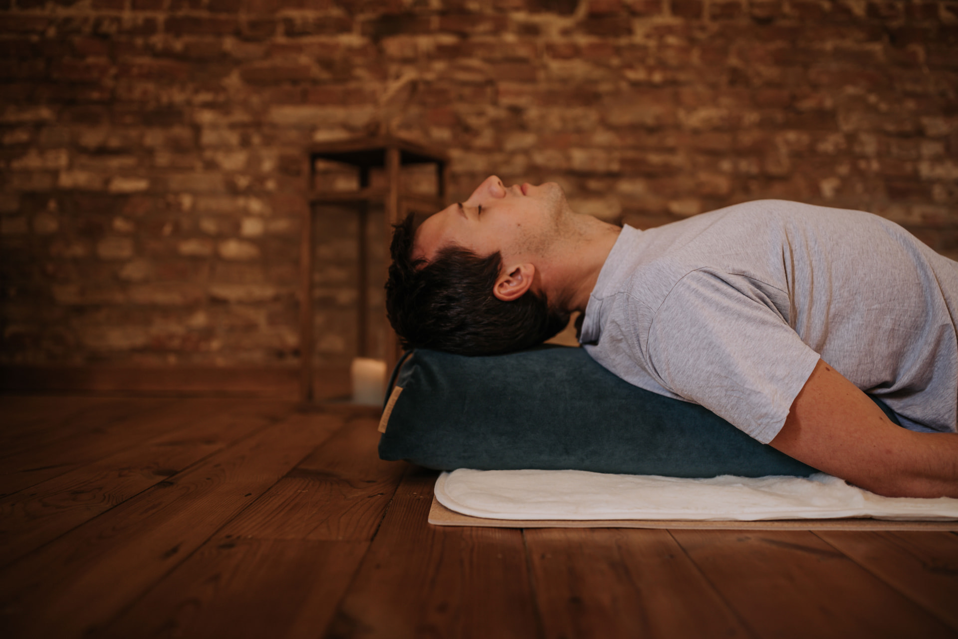 Person lying back over a teal PIERRE bolster on a wooden floor