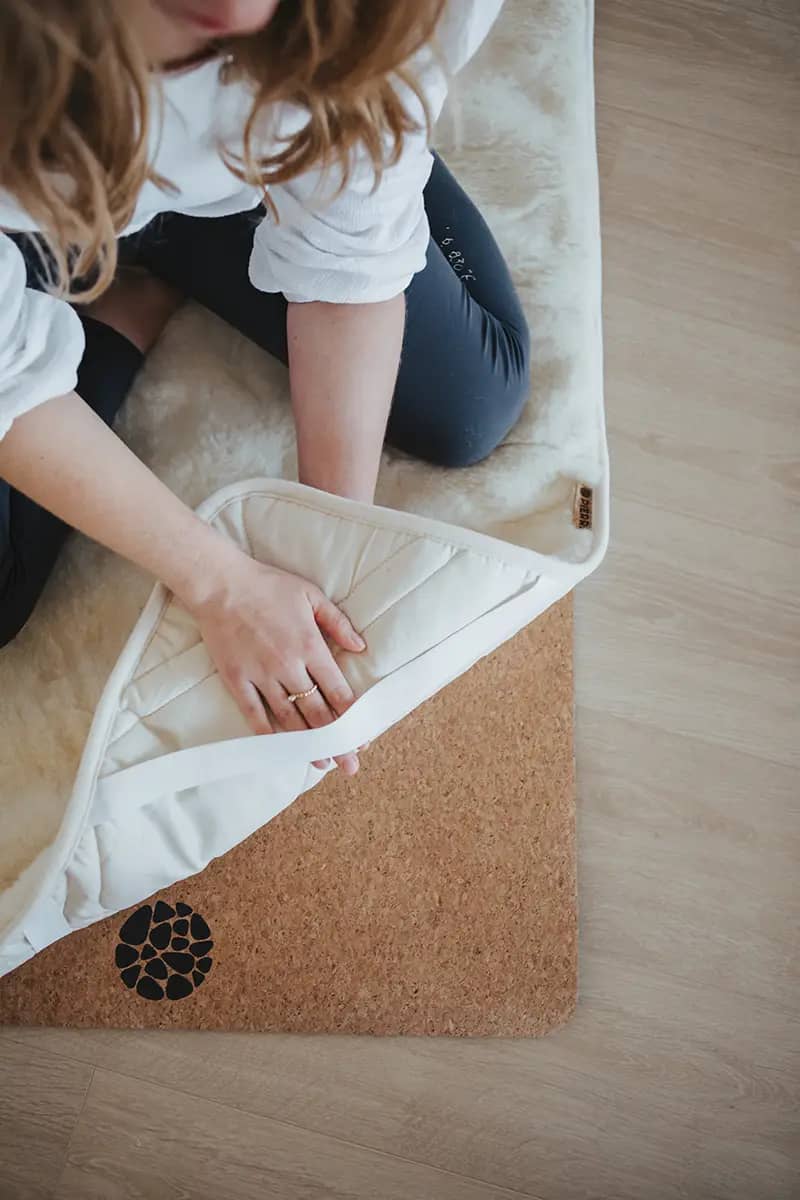 Hands folding back a cream wool cover to show the cork yoga mat underneath