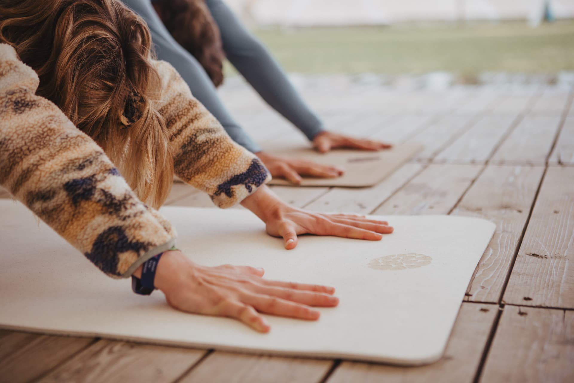 Close-up of hands pressing into a light cork yoga mat on a wooden deck