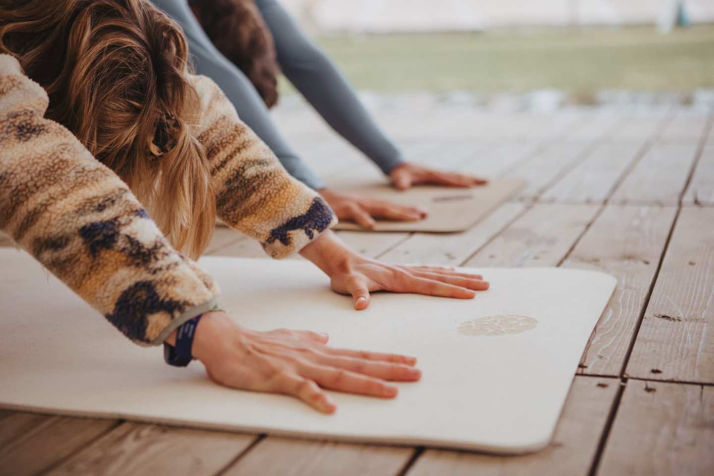 Close-up of hands pressing into a light cork yoga mat on a wooden deck