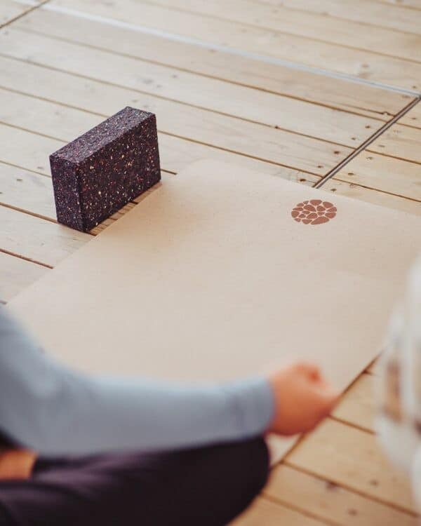 A close up of a Pierre Sports cork yoga mat and recycled foam yoga block setup on a light wooden floor for practice.
