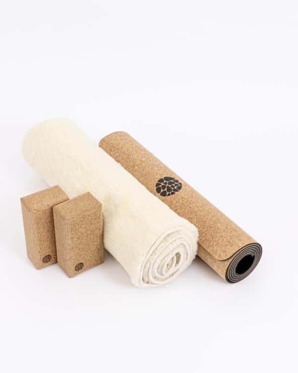 A rolled white wool yoga mat, a rolled natural cork yoga mat, and two Pierre Sports cork blocks on a white background.